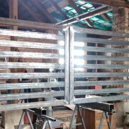 STAR-SPAW Ziejka Mariusz - Surowa, metalowa brama dwuskrzydłowa w trakcie spawania, widoczne spawy, szlifowane elementy i surowy warsztat w tle.