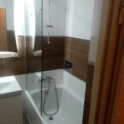 Nowoczesna łazienka z brązowo-białymi płytkami, szklanym parawanem nawannowym i chromowaną armaturą.