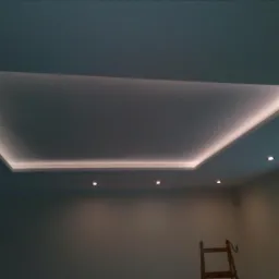 Podwieszany sufit z oświetleniem LED w kształcie prostokąta, uzupełniony punktowymi lampami halogenowymi, widoczna drabina w rogu pokoju.