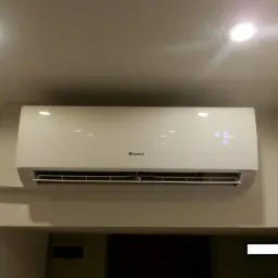 Biała jednostka klimatyzacyjna Gree zamontowana na ścianie nad drzwiami, wyświetlająca temperaturę 16 stopni Celsjusza, oświetlona dwoma punktowymi lampami sufitowymi.