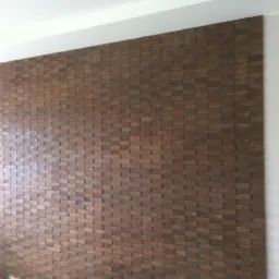 Dekoracyjna ściana z drewnianych, trójwymiarowych paneli w odcieniach brązu, tworzących unikalną teksturę w nowoczesnym wnętrzu z białymi ścianami.