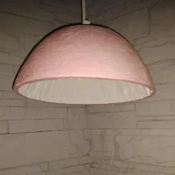 Różowa lampa wisząca z papierowym kloszem o teksturowanej powierzchni, zawieszona w rogu pomieszczenia z dekoracyjną ścianą z kamiennych płytek.