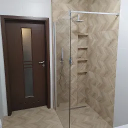 Nowoczesna kabina prysznicowa z deszczownicą i wnękami w ścianie, wyłożona płytkami w jodełkę, obok ciemne drewniane drzwi z przeszkleniem.