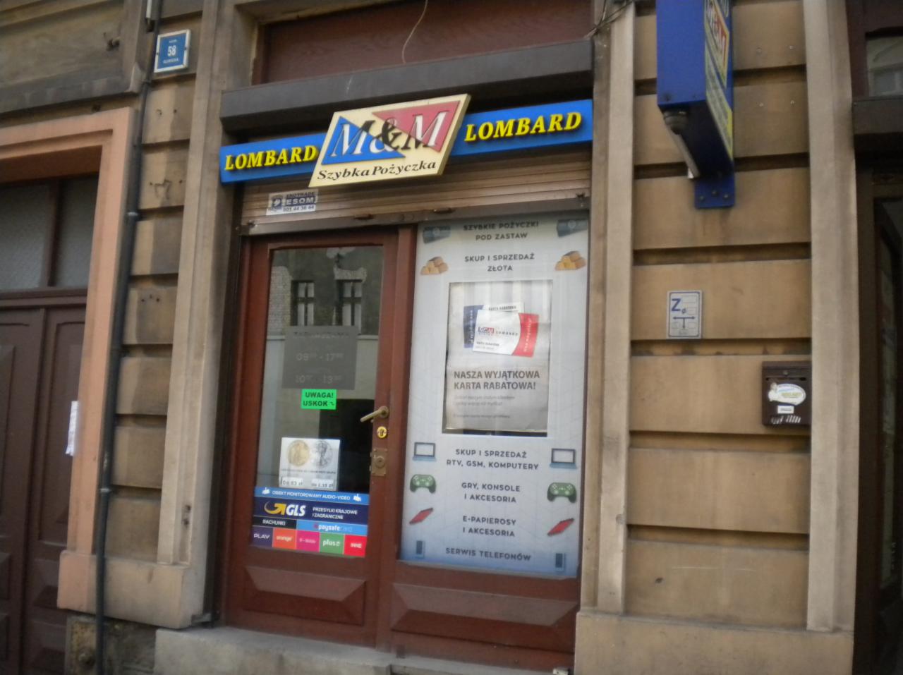 Fasada lombardu M&M z szyldem, informacjami o skupie złota, elektroniki, kartach rabatowych i serwisie telefonów, umieszczonymi na drzwiach wejściowych.