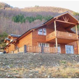 Tatran 3R Sp. z o.o. - Drewniany dom z balkonem na tle zalesionego wzgórza. Widoczne detale konstrukcyjne i naturalna kolorystyka drewna. Ujęcie z dołu podkreśla bryłę budynku.