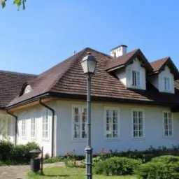 Odrestaurowany, parterowy budynek z brązowym dachem krytym dachówką, białą elewacją i symetrycznie rozmieszczonymi oknami, oświetlony przez klasyczną latarnię uliczną na pierwszym planie.