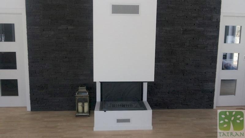 Nowoczesny kominek z białym obramowaniem na tle ściany z czarnego kamienia łupkowego, oświetlony lampionem ze świecami, pomiędzy białymi drzwiami z przeszkleniami.