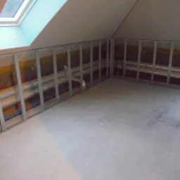 Stelaż z profili metalowych pod zabudowę z płyt karton-gips na poddaszu, widoczne rury instalacyjne za stelażem, okno dachowe w skosie.