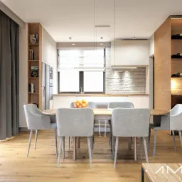 Jasna jadalnia z okrągłym stołem i szarymi krzesłami na drewnianej podłodze, w tle kuchnia z ceglaną ścianą i półki na wino z podświetleniem.