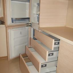 P.h.u.laskar - Jasna szafa na wymiar z trzema wysuwanymi szufladami z frontami z jasnego drewna, zintegrowana z lodówką, widoczne logo 'MB' na szufladach.