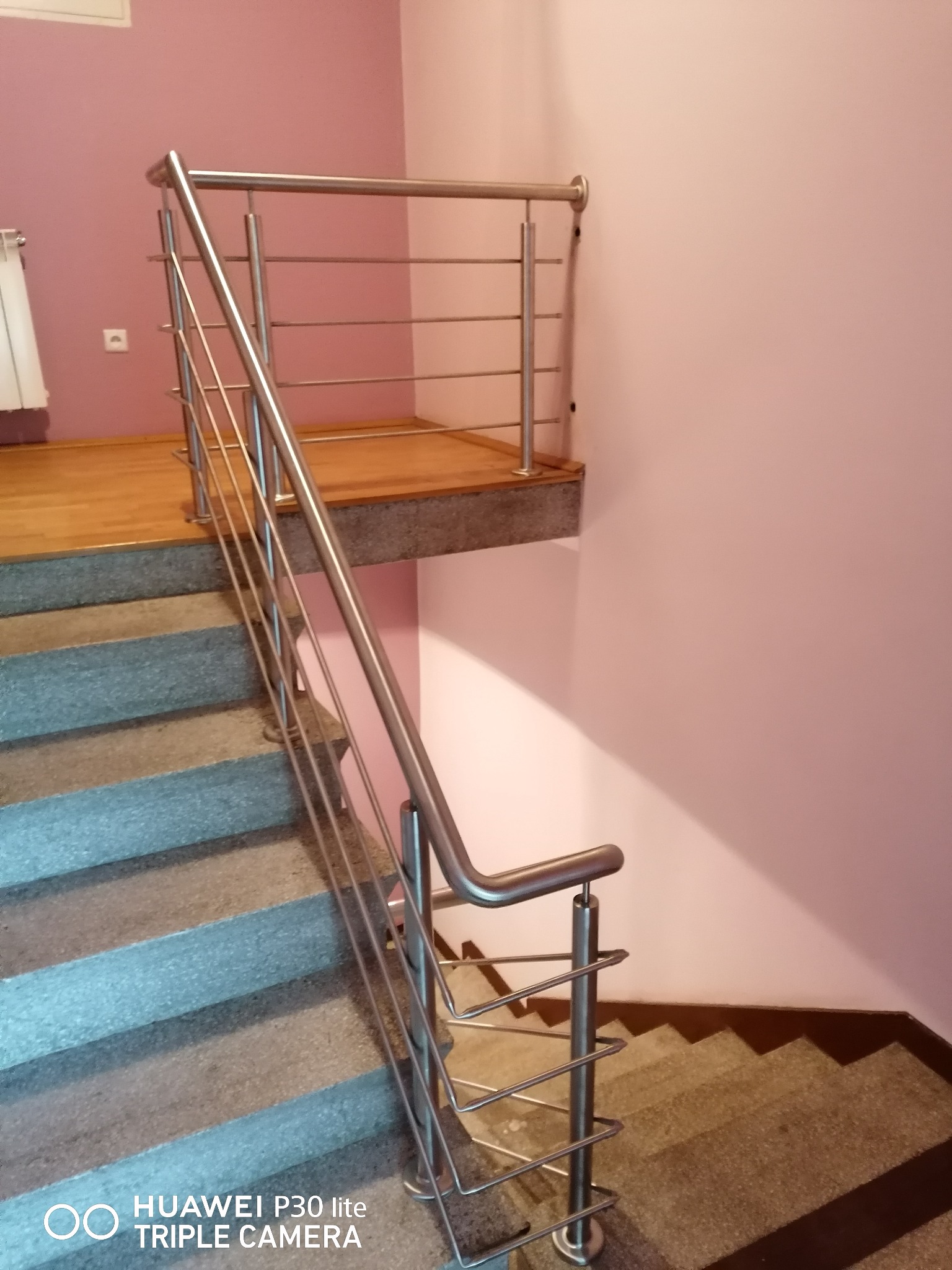 Schody betonowe z nowoczesną, metalową poręczą z poziomymi prętami, ściana w odcieniu pudrowego różu, widok z dołu.