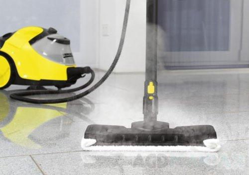 Żółto-szary parowy mop czyszczący Karcher w trakcie pracy na marmurowej podłodze, widoczna para.
