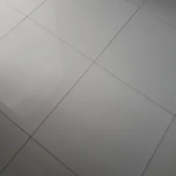 Błyszcząca, jasnoszara podłoga wyłożona kwadratowymi płytkami, z ciemnoszarymi fugami, sfotografowana pod kątem.