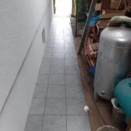 Wyłożona szarymi płytkami wąska ścieżka między ścianą budynku a zagraconym podwórkiem, widok w perspektywie.