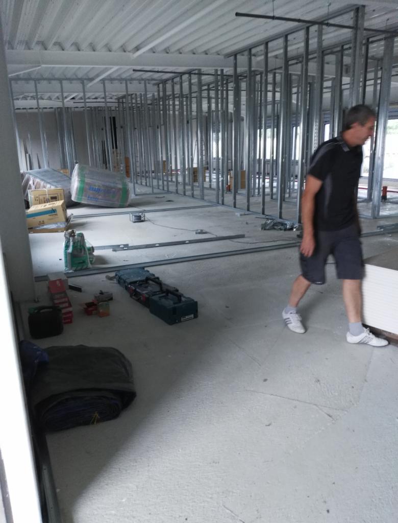 Montaż metalowej konstrukcji ścian działowych z płyt kartonowo-gipsowych w surowym stanie, widoczny pracownik w trakcie pracy.