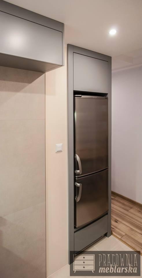 Szara zabudowa kuchenna na wymiar z lodówką w stalowym wykończeniu, widoczny fragment podłogi z paneli i logo firmy meblarskiej w rogu.