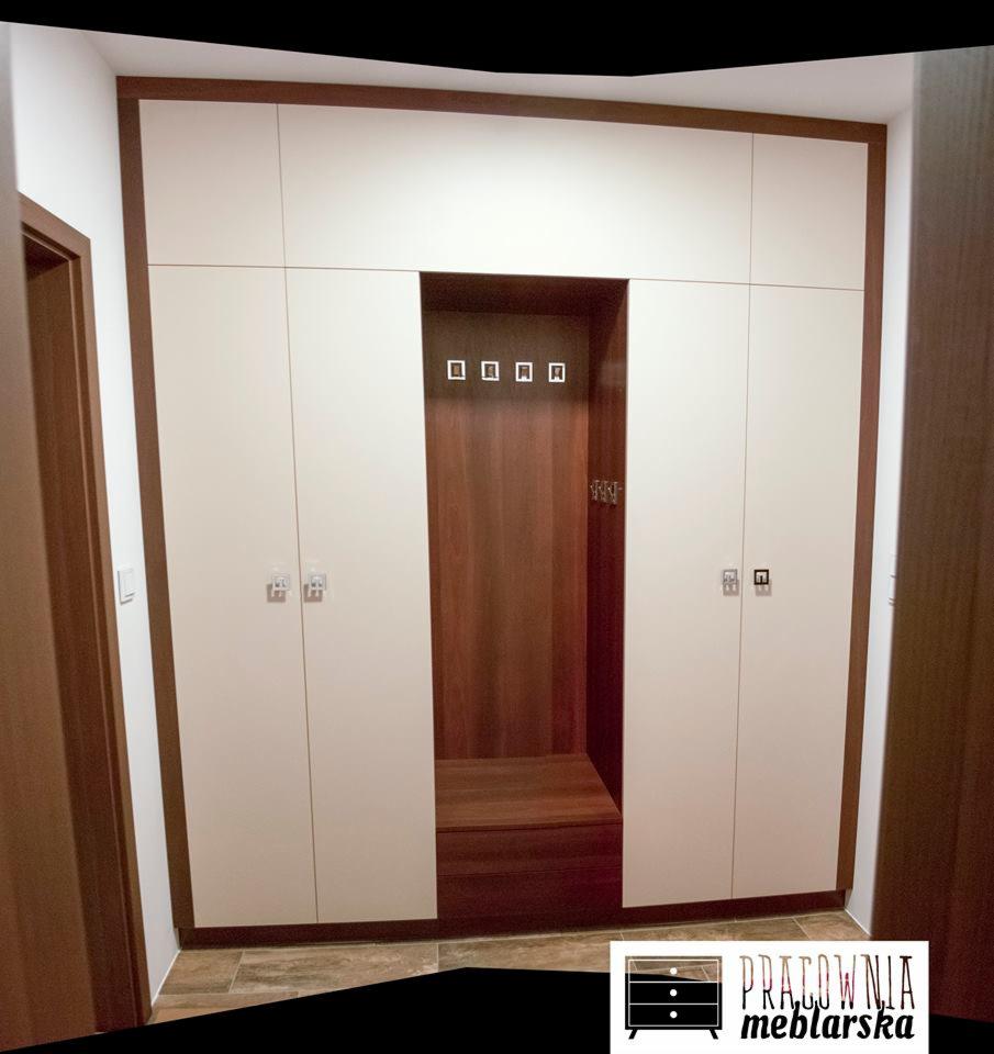 Biała szafa wnękowa z siedziskiem i wieszakami w przedpokoju, wykończona drewnem w ciepłym odcieniu brązu.