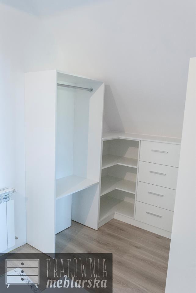 Biała zabudowa wnęki pod skosem z drążkiem na ubrania, półkami narożnymi i szafką z szufladami, widoczna część logo firmy meblarskiej.