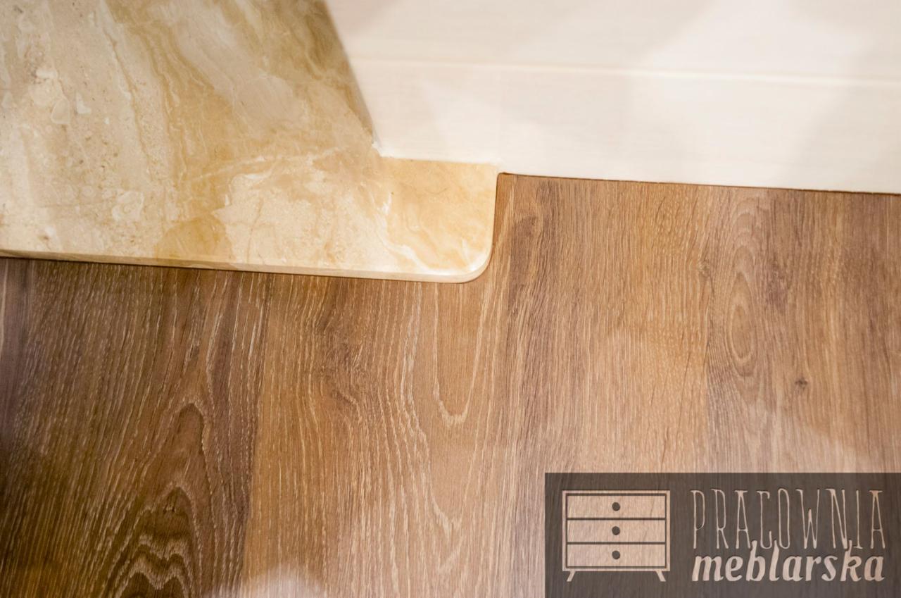 Fragment blatu z jasnego marmuru, przylegającego do drewnopodobnej powierzchni. W prawym dolnym rogu widoczne logo 'Pracownia Meblarska'.