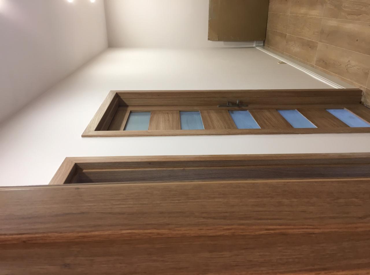 Dwa drewniane ościeżnice i drzwi z szybami w tle, widok z dołu, jasne wnętrze.