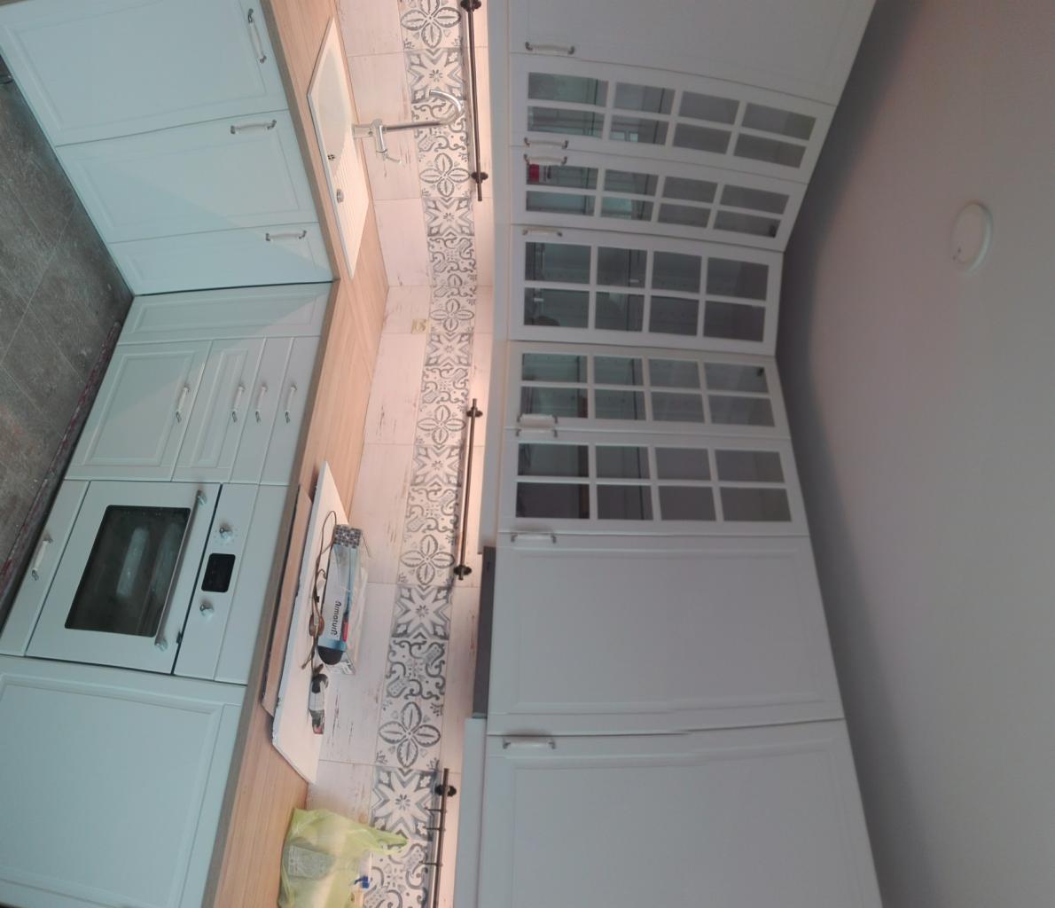 Nowoczesna biała kuchnia z szafkami z przeszklonymi frontami i dekoracyjnymi płytkami nad blatem.