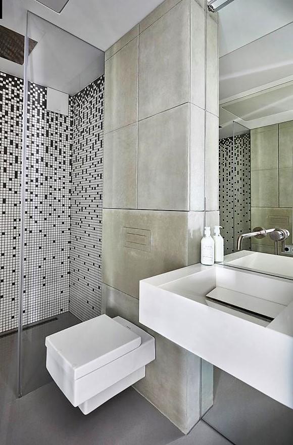 Nowoczesna łazienka z kabiną prysznicową wykończoną mozaiką w czarno-białą kratkę, betonową kolumną i umywalką o geometrycznym kształcie.