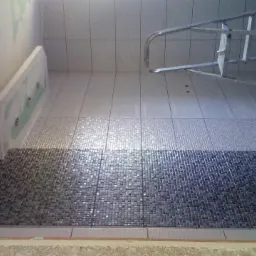 Ściana łazienki w trakcie remontu z ułożoną mozaiką w odcieniach szarości i bieli, widoczna drabina aluminiowa i surowy stan ścian