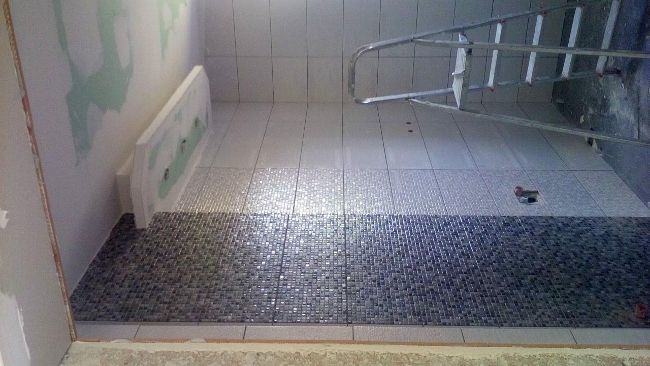 Ściana łazienki w trakcie remontu z ułożoną mozaiką w odcieniach szarości i bieli, widoczna drabina aluminiowa i surowy stan ścian