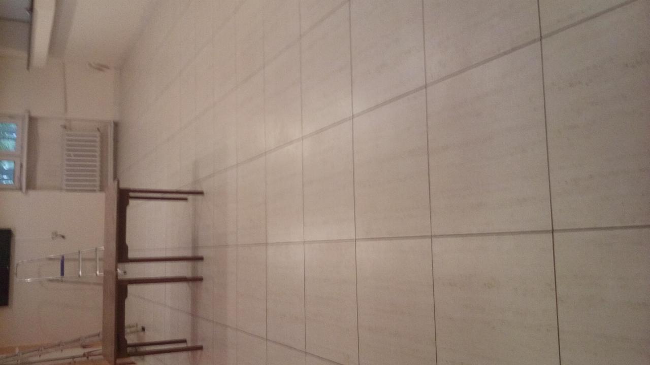 Ściana wyłożona dużymi, beżowymi płytkami imitującymi kamień, widoczny grzejnik drabinkowy i fragment drabiny, wnętrze w trakcie prac.