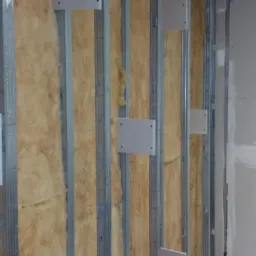 Konstrukcja ścian działowych z profili stalowych wypełniona wełną mineralną, przygotowana do montażu płyt gipsowo-kartonowych, widoczne metalowe mocowania.