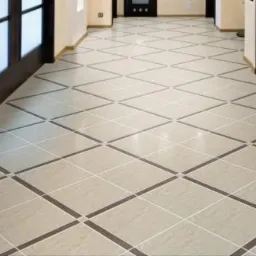 Beżowa podłoga z płytek ułożonych w romby z ciemnobrązowymi akcentami, widok z perspektywy wejścia do pomieszczenia z przeszklonymi drzwiami.