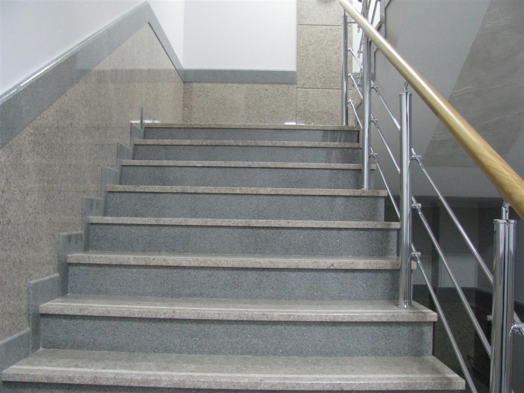 Kamienne schody w odcieniach szarości z chromowanymi barierkami i drewnianym poręczą, zrealizowane w Krakowie.