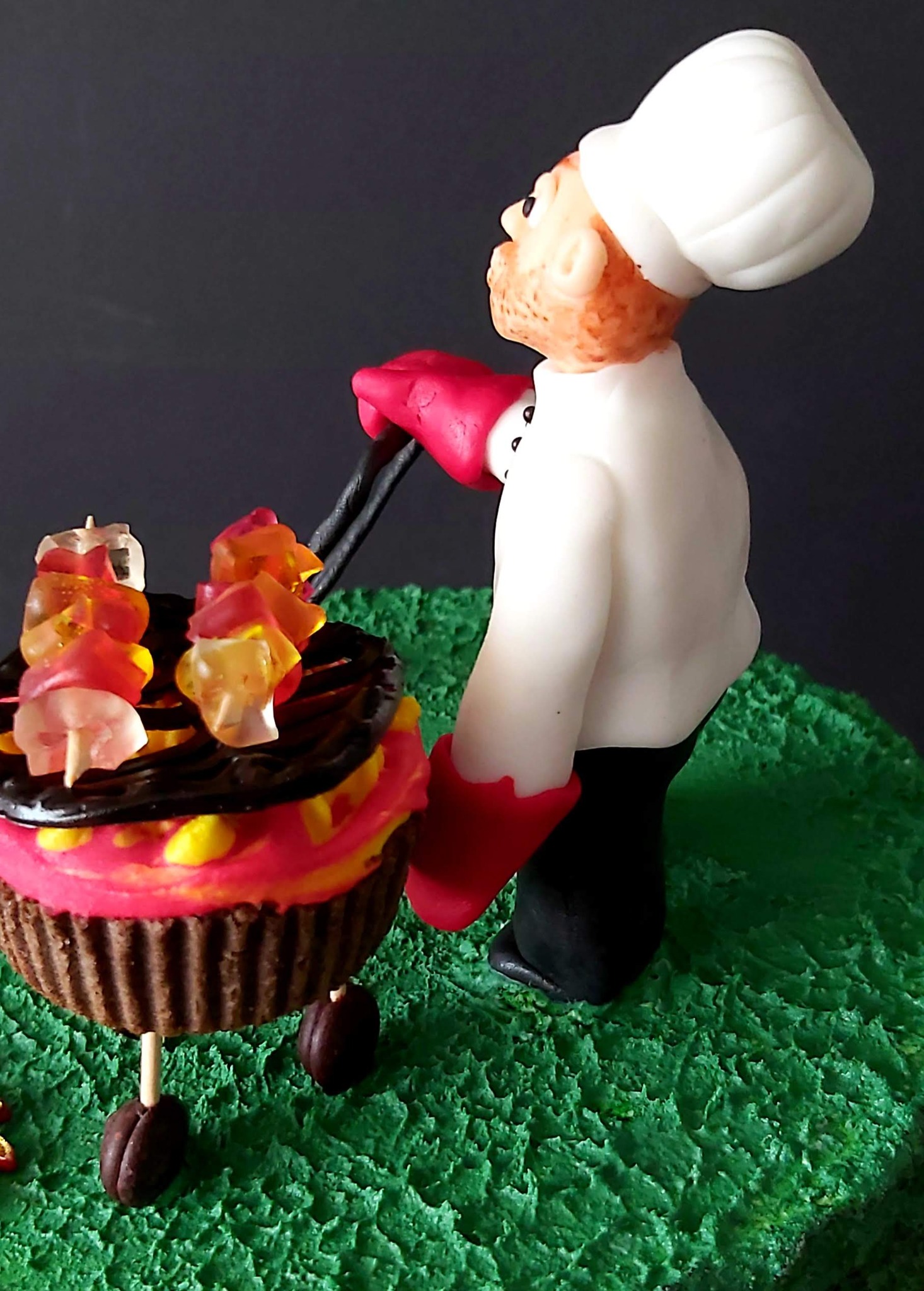 Dekoracyjny tort w formie grilla z figurką kucharza w czapce i rękawicach, przygotowującego szaszłyki z żelków.