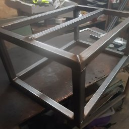 HARAZIN Michał Harazin - Spawana, metalowa rama o regularnej strukturze, z widocznymi śladami spawania, umieszczona na warsztatowym stole. Surowy, industrialny charakter, detale połączeń.