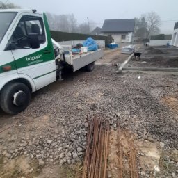 HARAZIN Michał Harazin - Teren budowy w trakcie przygotowania fundamentów: żwir, zbrojenia, częściowo zalany fundament, w tle budynek i auto dostawcze z logo firmy.