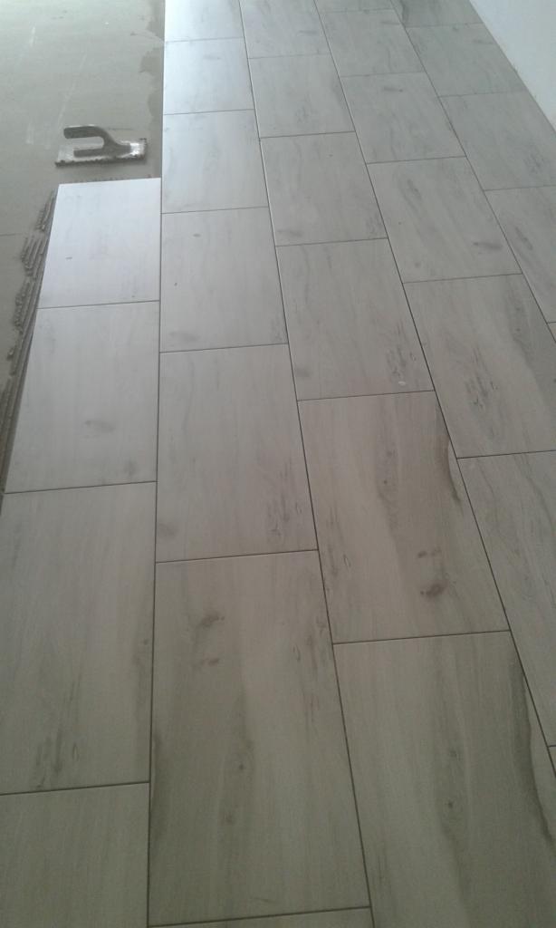 Ułożone płytki podłogowe imitujące drewno w odcieniach szarości, widoczna szpachelka i fragment podłoża przed położeniem płytek.