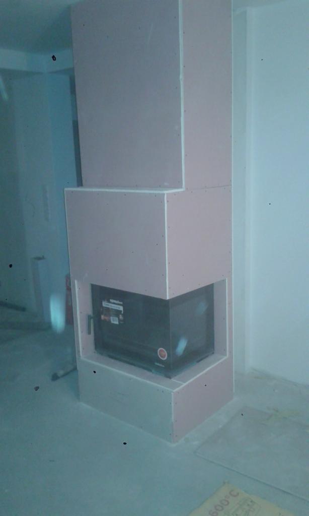 Konstrukcja kominka z płyt gipsowo-kartonowych w trakcie montażu, widoczne łączenia i wkręty, surowy stan wykończenia wnętrza.