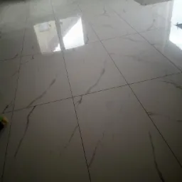 Ułożona podłoga z białych płytek imitujących marmur z szarymi żyłami, widoczne odbicia światła, w tle materiały budowlane i narzędzia.