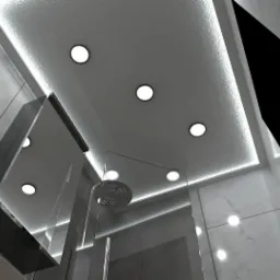 Nowoczesna łazienka z marmurowymi płytkami, szklaną kabiną prysznicową i oświetleniem punktowym w suficie podwieszanym, widok z dołu.