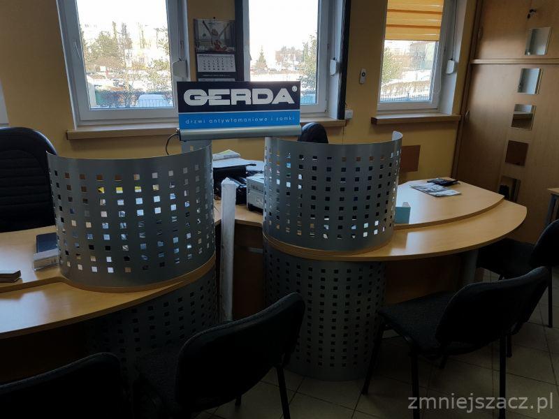 Biuro z dwoma stanowiskami obsługi klienta oddzielonymi metalowymi, ażurowymi przegrodami, na monitorze widoczne logo firmy Gerda.