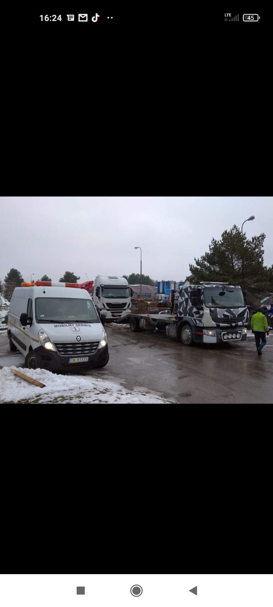 Renault Master 'Mobilny Serwis' z pomarańczowymi światłami ostrzegawczymi, Iveco Eurocargo i ciężarówka z kamuflażem na parkingu w zimowy dzień.