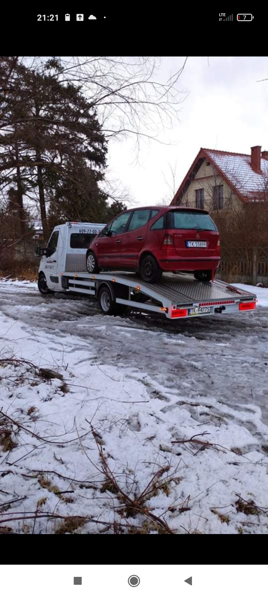 Czerwony samochód osobowy Mercedes A-klasa przewożony na lawecie w zimowych warunkach, z widocznym numerem telefonu na kabinie holownika.
