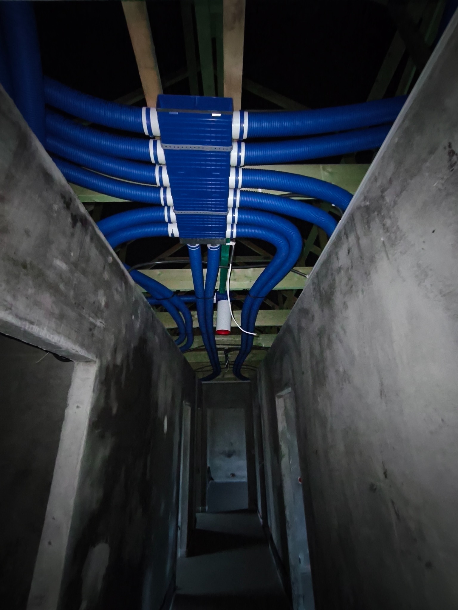 Niebieskie rury wentylacyjne z białymi paskami, rozprowadzone pod sufitem w surowym wnętrzu budynku w trakcie budowy.