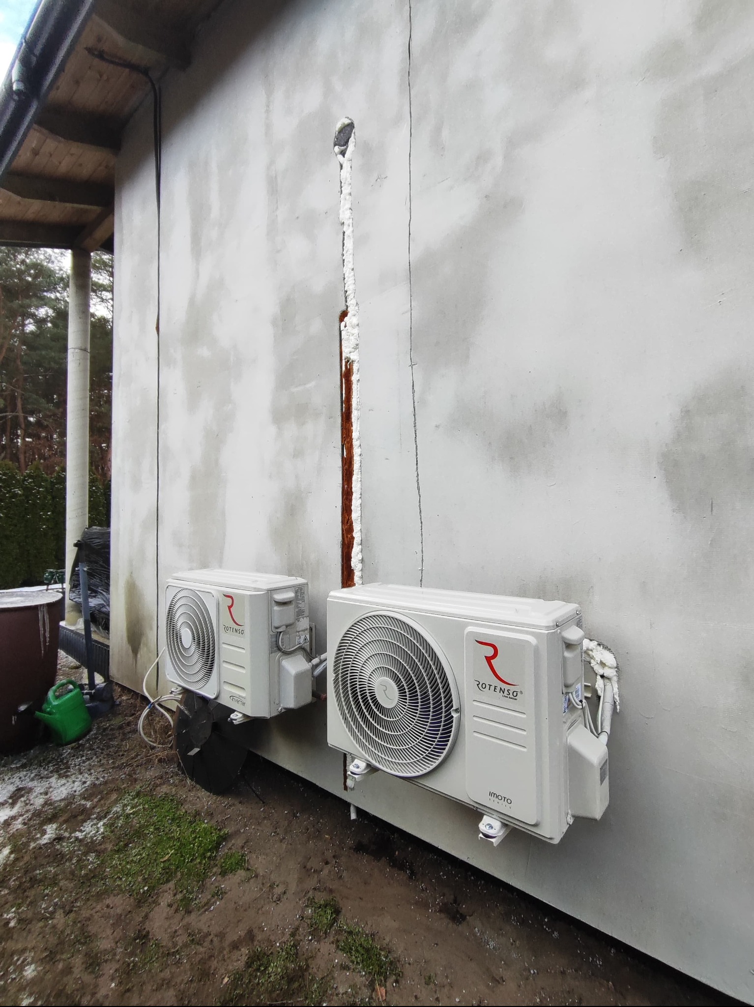 Dwa klimatyzatory Rotenso zamontowane na surowej ścianie budynku z widoczną pianką montażową wokół przewiertu i śladami po instalacji.