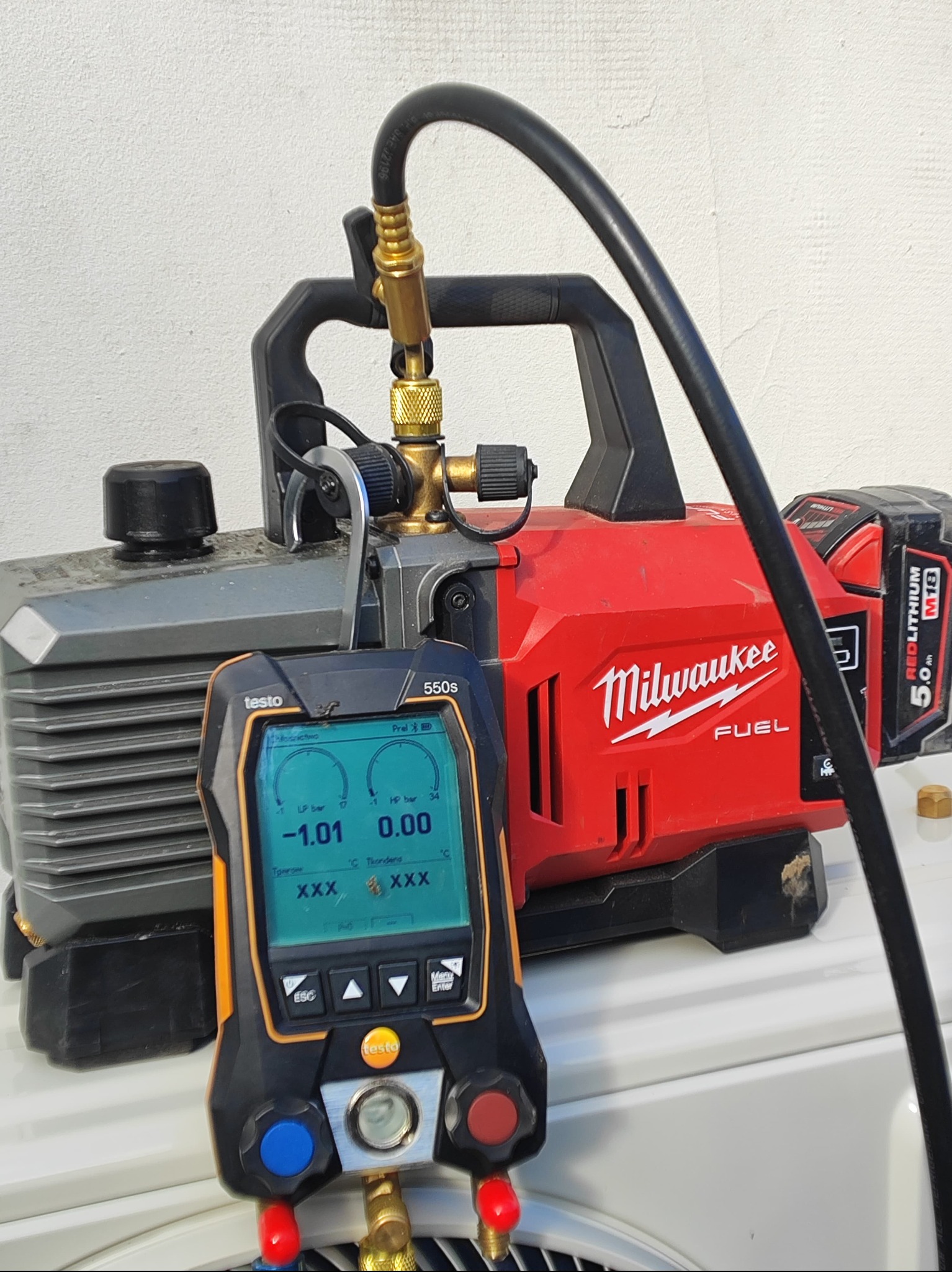 Podłączenie cyfrowego manometru Testo 550s do pompy próżniowej Milwaukee Fuel z akumulatorem 5.0 Ah, widoczne wskazania ciśnienia na wyświetlaczu.