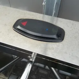 Zbliżenie na czytnik kart dostępu z sygnalizacją LED (czerwone strzałki w górę i niebieska dioda) umieszczony na metalowej obudowie bramki obrotowej.