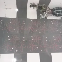 Podłoga w łazience wyłożona szarymi płytkami z motywem kwiatowym w kolorze różowym, ułożonymi na przemian z białymi i czarnymi płytkami, z dekoracyjnym wazonem z kwiatami i akcesoriami łazienkowymi...