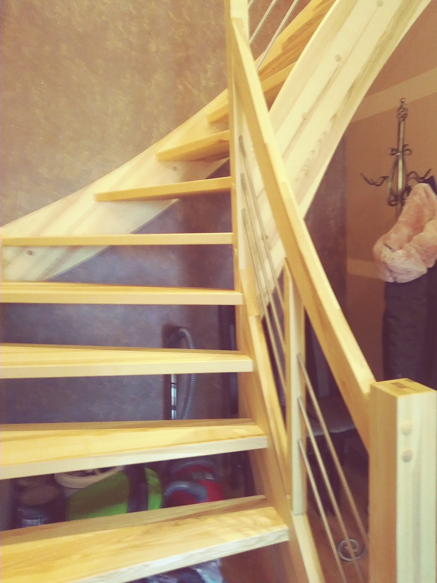 Spiralne schody z jasnego drewna z metalowymi poręczami, widok z dołu, z widocznymi przedmiotami pod schodami.