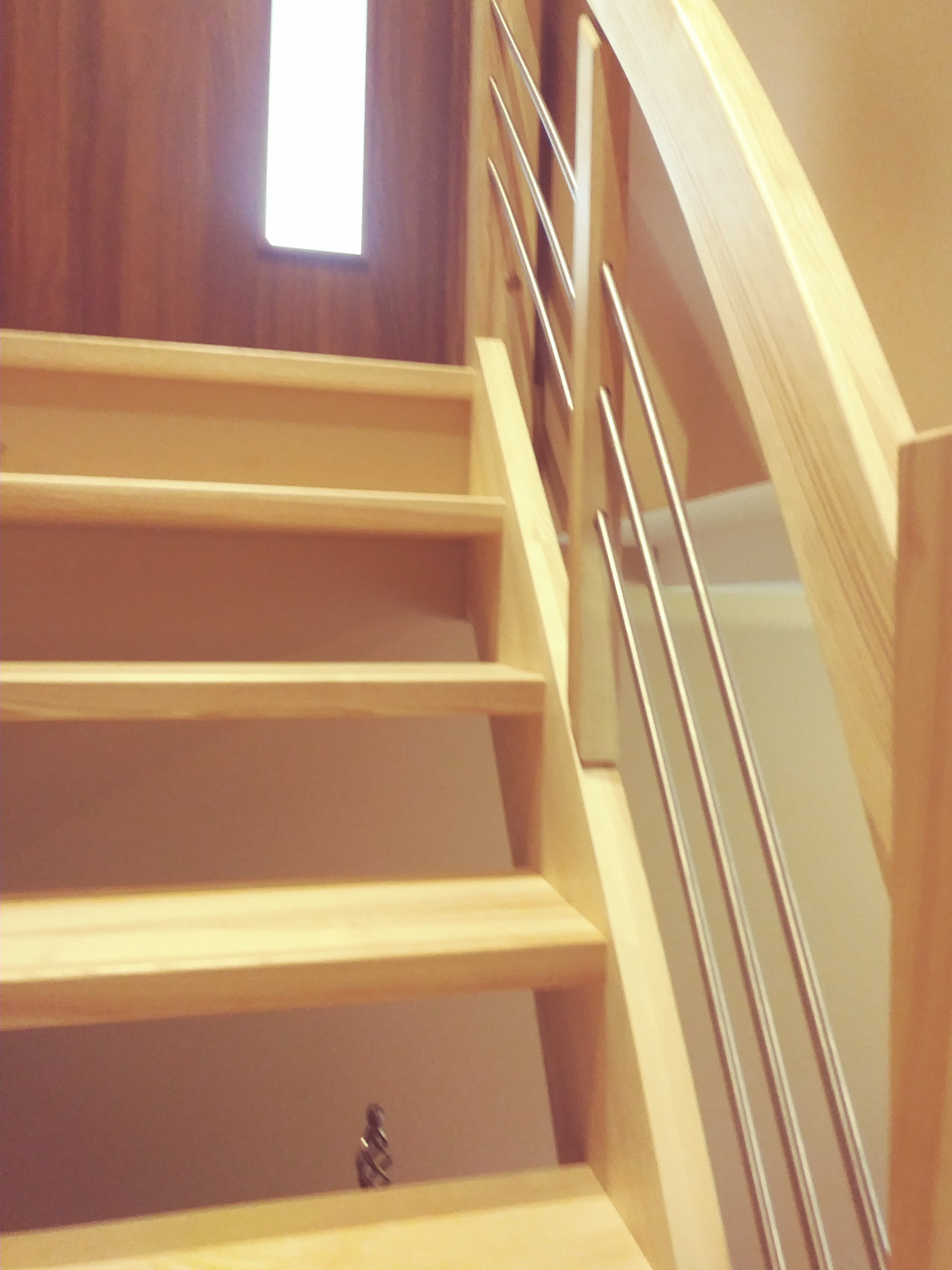 Jasne drewniane schody z metalowymi poręczami, oświetlone przez okno w tle, widok z dołu.