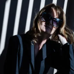 Portret kobiety w czarnym żakiecie i okularach przeciwsłonecznych, oświetlonej prążkami światła, wykonany w Zbrudzewie.